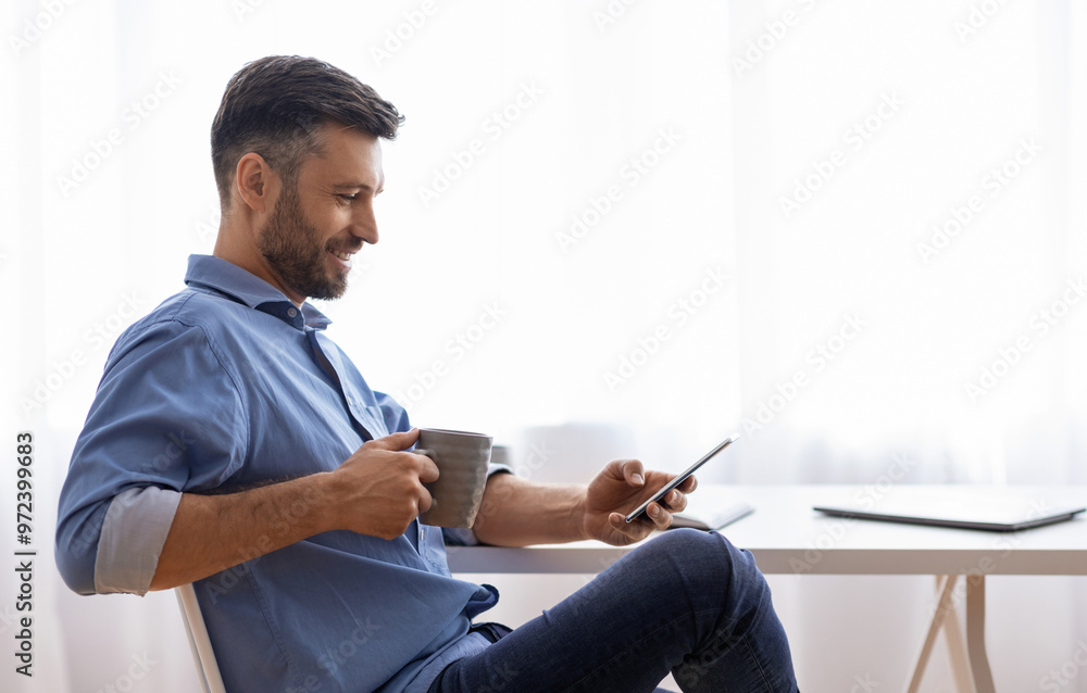 Poster break in work. relaxed male freelancer using smartphone and drinking coffee while sitting at desk at