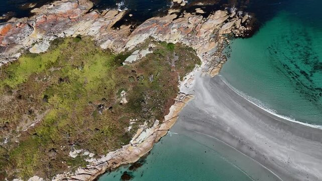 Tilting drone shot shows the granite cliffs and white sand beach of Bicheno Island in Tasmania.