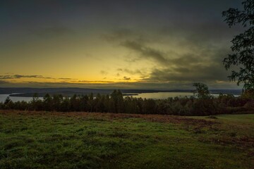 Serene landscape with grassy field, trees, and lake at sunset.