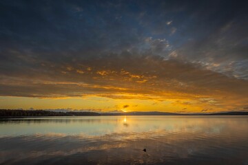 Sunset over a calm lake with dramatic sky.