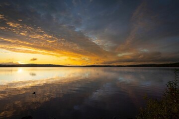 Obraz premium Sunset over a calm lake with dramatic clouds and reflections.