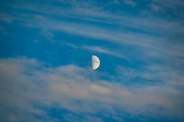 Blue sky with clouds and a small crescent moon in the middle.