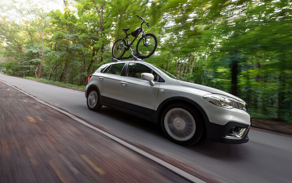 Motion shot of white Suzuki crossover. Suzuki SX-4 driving in a green forest with a bicycle on a roof rack. Low angle view of the right side. Kyiv, Ukraine - August 07 2019.	