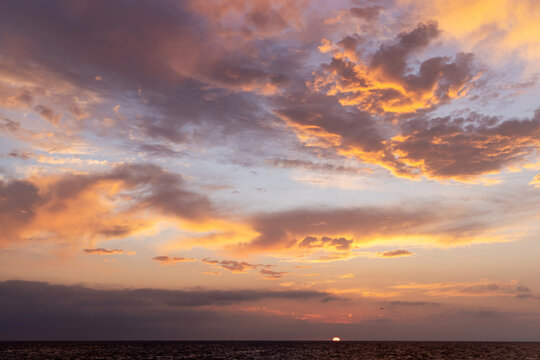 A dramatic and moody sunset sky filled with dark, swirling clouds