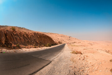 A winding road through the arid landscape of Jordan’s Nature reserves under a clear blue sky in the early afternoon