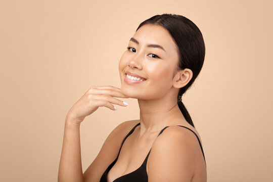 Facial Beauty Care. Portrait Of Happy Japanese Young Lady Touching Her Face And Chin Skin Over Gray Background In Studio, Smiling To Camera. Woman Advertising Double Chin Treatment Concept