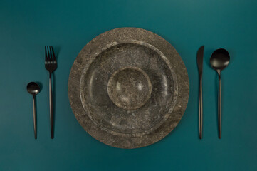 Top view of brown marble tray and plate, black cutlery on dark green background. Food presentation,...