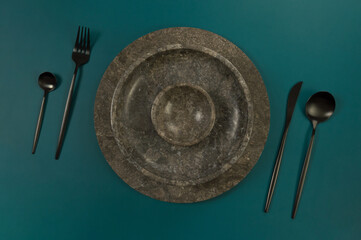 Top view of brown marble tray and plate, black cutlery on dark green background. Food presentation,...