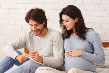 Choosing Baby Name. Young pregnant couple naming their future child, writing options to notebook...