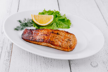 Grilled salmon steak lying on white plate with lemon and lettuce
