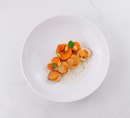 Seared scallops plate garnished with carrot and pistachio being served in a restaurant