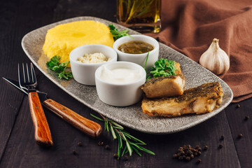 Fried fish fillet served on plate with polenta and sauces
