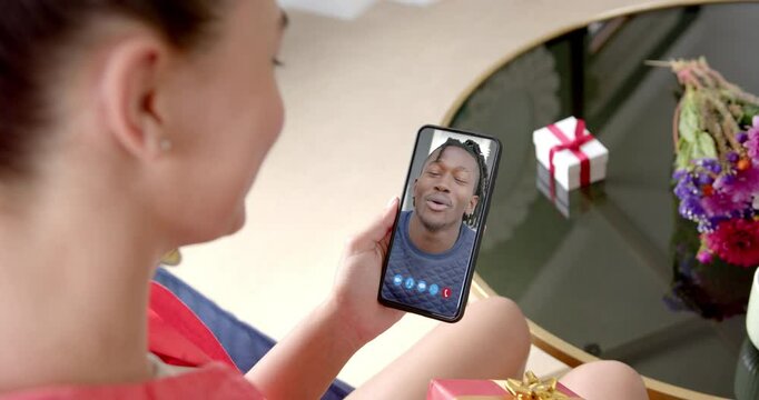 Biracial woman holding smartphone with african american manon screen with gift on desk