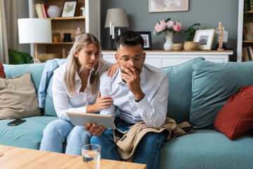 Young businesswoman comforting her husband at home while he reading negative statistics of his business company trade on digital tablet. Togetherness and emotional support.