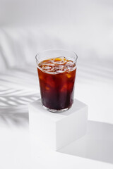 Cold brew coffee standing on white cube with tropical plant shadow