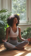 A Black woman meditating in her home, surrounded by plants and natural light streaming through the window