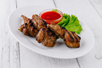 Grilled lamb chops served on white plate with spicy tomato sauce and salad