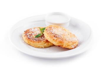 Two golden brown cheese pancakes lying on white plate with sour cream and mint