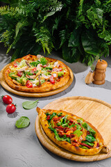 Caesar salad pizza and turkish pide lying on wooden boards