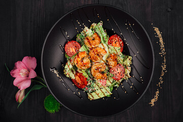 Delicious salad with shrimps and tomatoes lying on black table