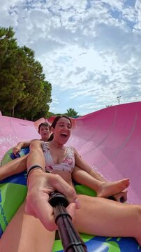 Selfie of son and mother having fun, going down a water tube on a rubber ring. Sliding at a Water Amusement Park on summer vacation. Vertical 4k video