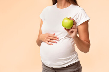 Unrecognizable Pregnant Lady Showing Apple Touching Belly Posing Over White Background. Healthy Eating During Pregnancy. Cropped