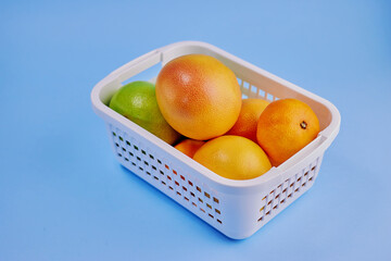 grapefruits, sweeties, tangerines lie inside a white plastic container on a blue background close-up