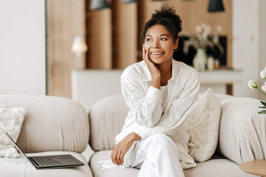 Beautiful young woman sitting on sofa with laptop thinking about future opportunities