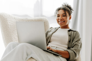 Young woman working from home sitting in armchair using laptop