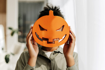Young boy hiding behind a scary pumpkin mask for halloween