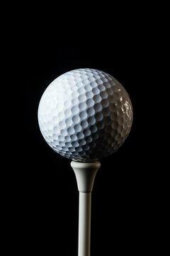 A white golf ball on a tee against a black background 