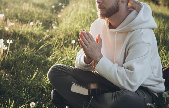 Man praying outdoors with a Bible on sunny day