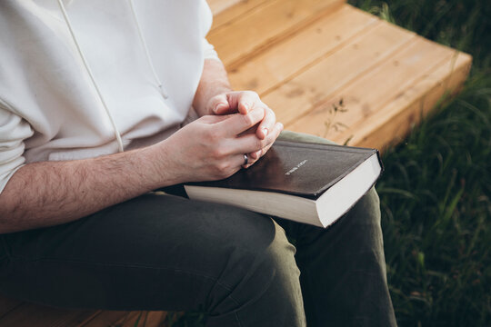Man reading Bible outdoors on a wooden bench