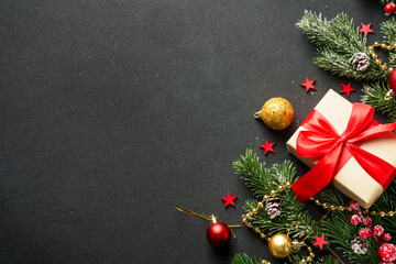 Christmas flat lay background. Present box, fir tree and holiday decorations on black.