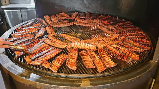 Barbecue ribs cooking on a circular smoker grill. A large circular smoker grill filled with rows of barbecue ribs sizzling over a fire.