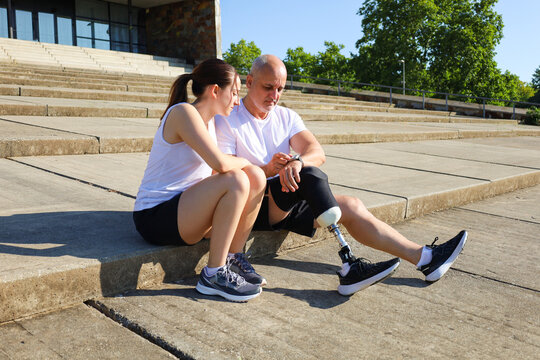 Supportive daughter and her father with a prosthetic leg resting outdoors - Powered by Adobe