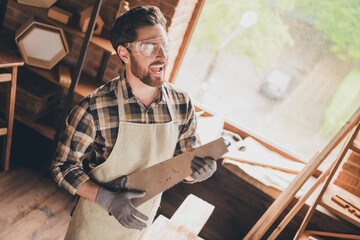 Photo of funny artisan guy builder playing saw blade imaginery guitar in garage indoors
