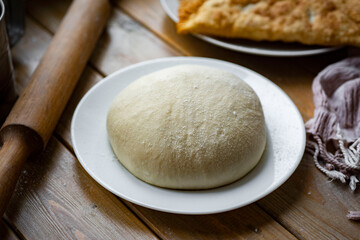 Dough on a plate on a wooden background. The dough is in the shape of a ball on a white plate on a wooden table. Close-up