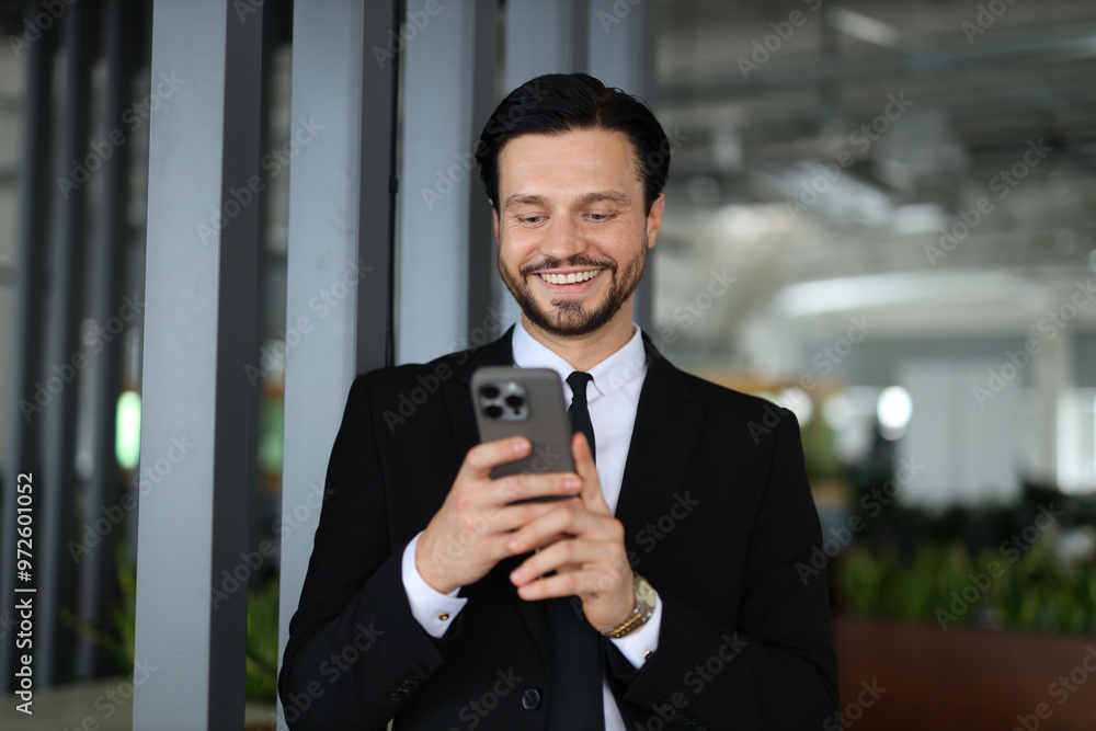 Poster a man in a suit is smiling while looking at his cell phone. he is wearing a tie and he is in a profe
