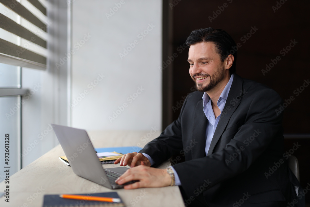 Poster a man in a suit is sitting at a desk with a laptop open in front of him. he is smiling and he is enj