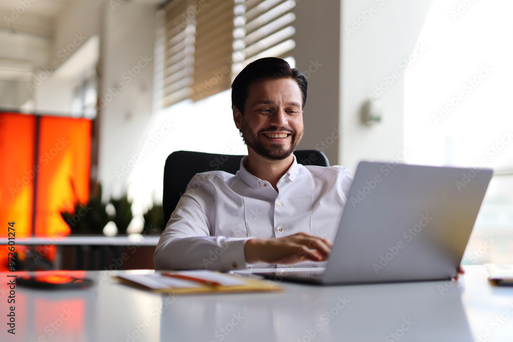 Poster a man is sitting at a desk with a laptop in front of him. he is smiling and he is enjoying his work