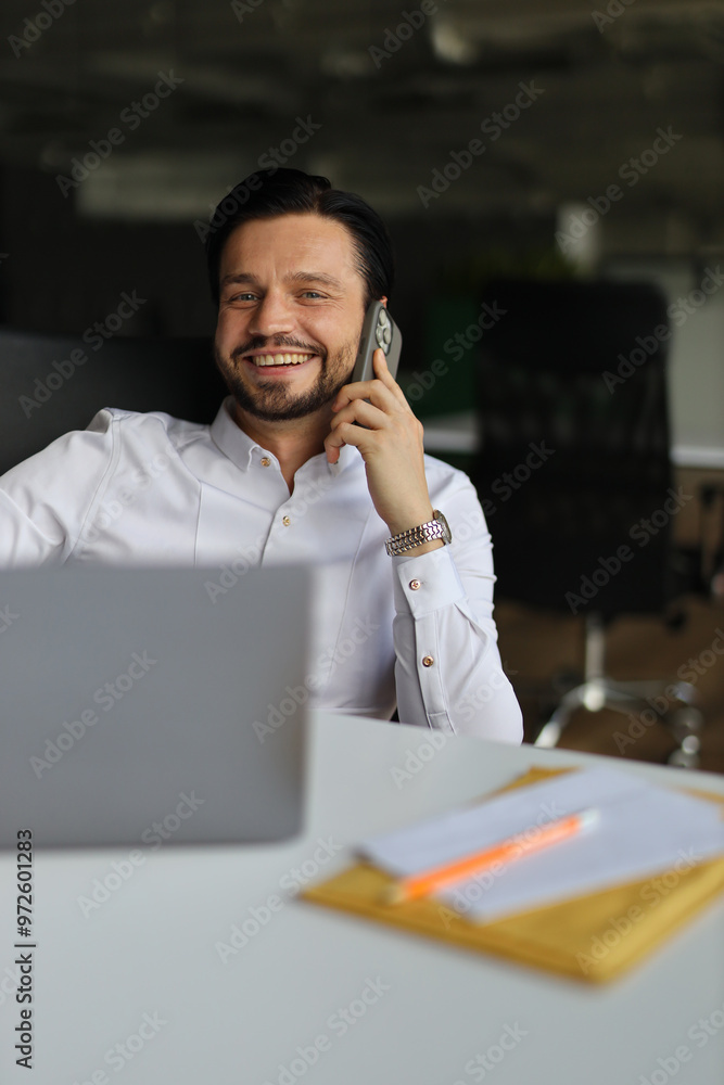Poster a man is talking on his cell phone while sitting at a desk. he is smiling and he is enjoying the con