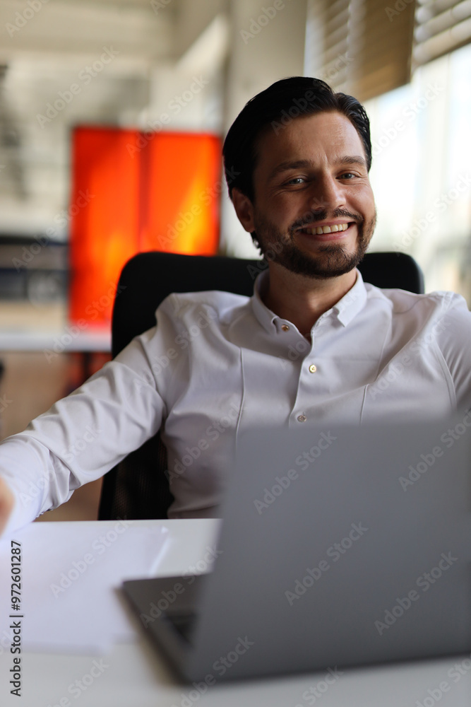 Poster a man is sitting at a desk with a laptop in front of him. he is smiling and he is happy