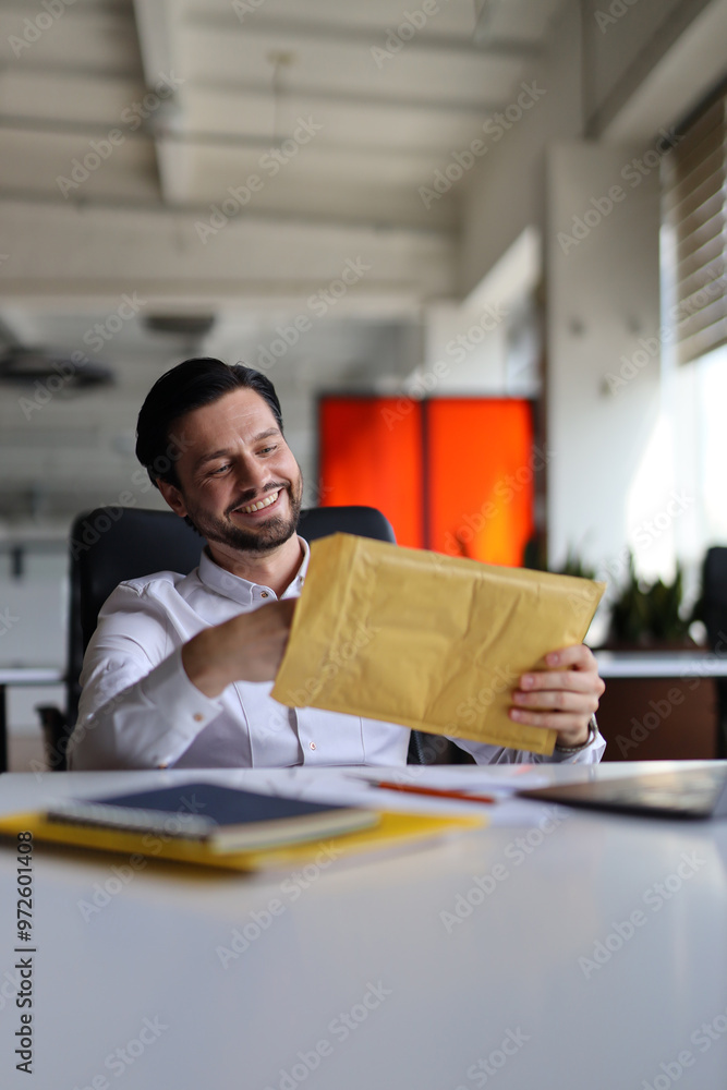 Poster a man is sitting at a desk with a yellow envelope in his hand. he is smiling and looking at the enve