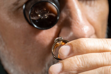Jewelry appraiser examines a gold ring evaluating large diamond looking through magnifying glass...