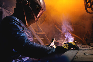A welder in a leather jacket and welding mask welds in a dark room of an old barn. Home welding