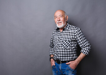 Obraz premium Serious senior man posing with hands on hips, gray studio background, copy space
