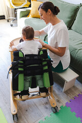 Small boy with muscle weakness practices standing in a rehabilitation device while physical...