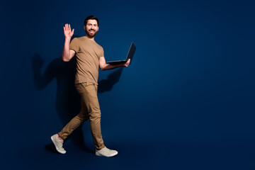 Photo of mature age web 3 developer brunet man with laptop walking waving hand friendly isolated on dark blue color background