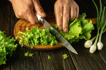 A chef uses a knife on a cutting board to cut lettuce leaves to prepare a vegetable dish for breakfast
